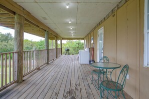 A covered porch with a wooden floor, a table with chairs, a washing machine, and a window. - Your Home Base in Southern Louisiana (Buras)