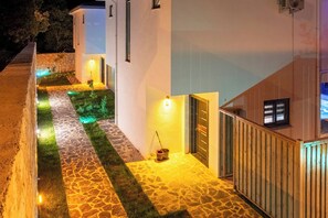 Uma passagem leva a um edifício com entrada em ladrilho de pedra e uma pequena área de jardim com grama sintética.