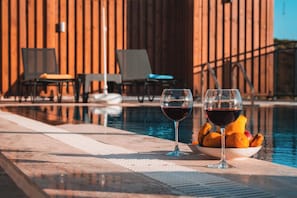 A poolside setting with two glasses of red wine and a bowl of fruit. - Villa savaya 1 Antalya (Kaş)
