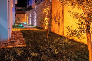 A nighttime outdoor area with a stone pathway, a small water feature, and a wall with decorative lighting. - Villa savaya 1 Antalya (Kaş)