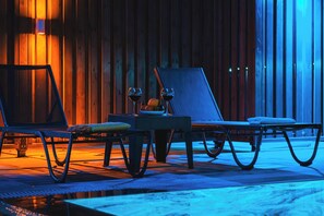 A lounge area with two lounge chairs, a table with a bowl of fruit, and a bottle of wine. - Villa savaya 1 Antalya (Kaş)