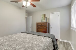 A bedroom with a bed, a wooden dresser, a ceiling fan, and a door. - Tiger Town Retreat: Spacious 2-Unit Combo! (Baton Rouge)