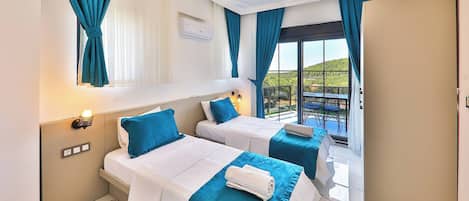 A hotel room with two beds, a balcony with a table and chairs, and a view of the landscape.