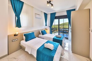 A hotel room with two beds, a balcony with a table and chairs, and a view of the landscape. - villa çınar-kaş Antalya (Kaş)