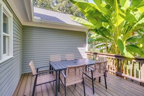 A wooden deck with a table and chairs, surrounded by a railing and large banana leaves. - Deck & Yard! Tri-City Family Home Near UNC & Duke (Chapel Hill)