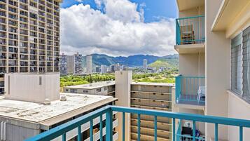 A multi-story building with balconies, a view of a cityscape, and mountains in the distance.