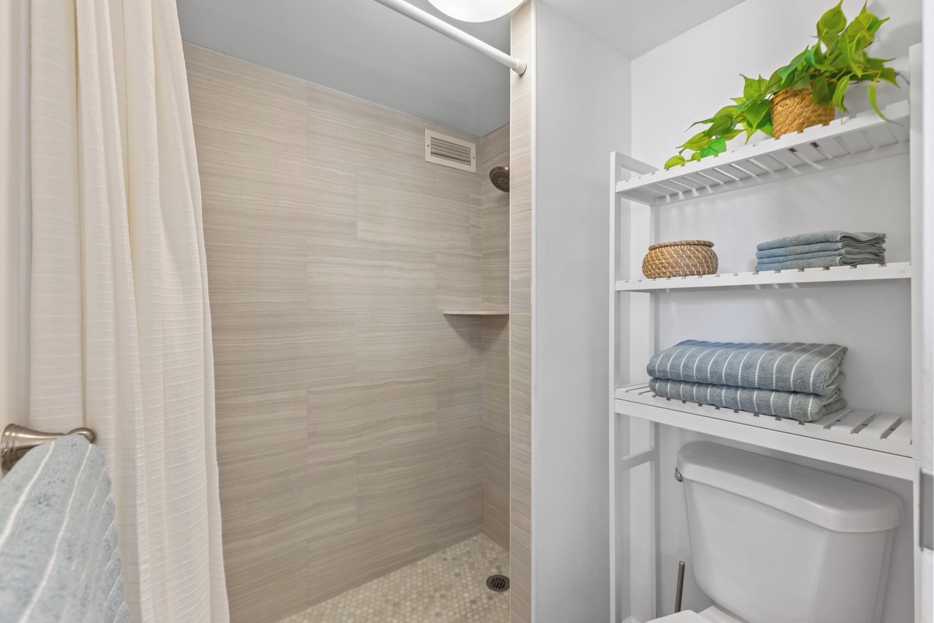 Un baño con ducha, inodoro y estantes con toallas y una planta.