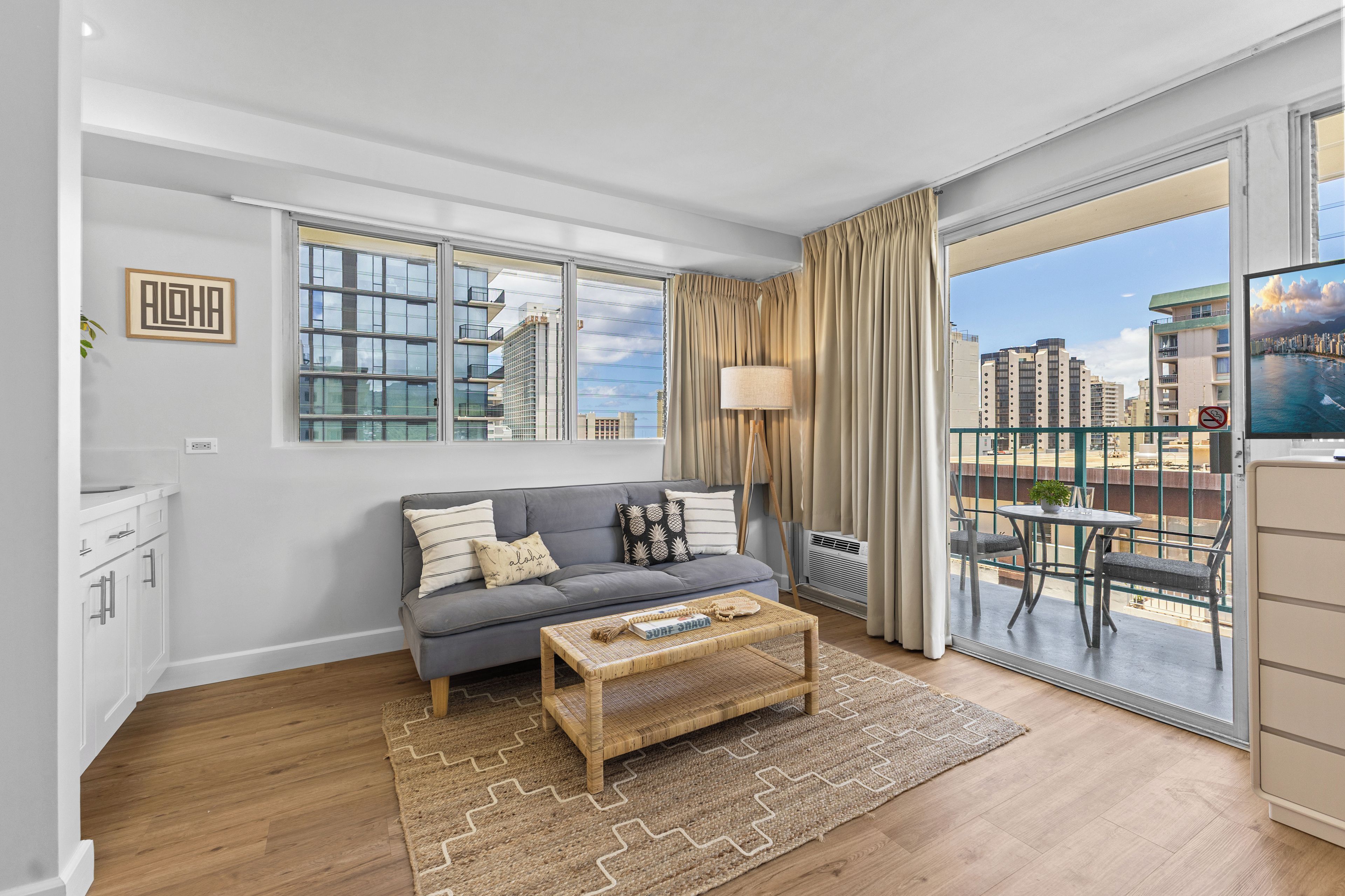 A modern living room with a grey sofa, a coffee table, and a view of a cityscape through large windows.