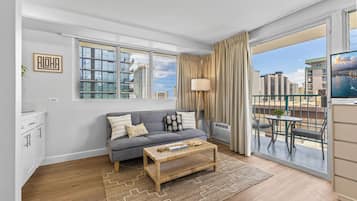 A modern living room with a grey sofa, a coffee table, and a view of a cityscape through large windows.