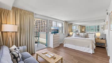 A hotel room with a balcony, a bed, a sofa, a TV, and a desk.