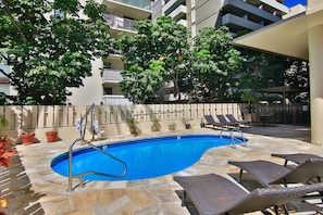 An outdoor swimming pool with lounge chairs and potted plants. - Newly renovated Waikiki Studios (Honolulu)