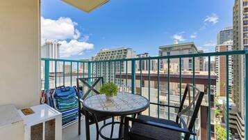 A balcony with a table and chairs, a potted plant, and a view of city buildings.