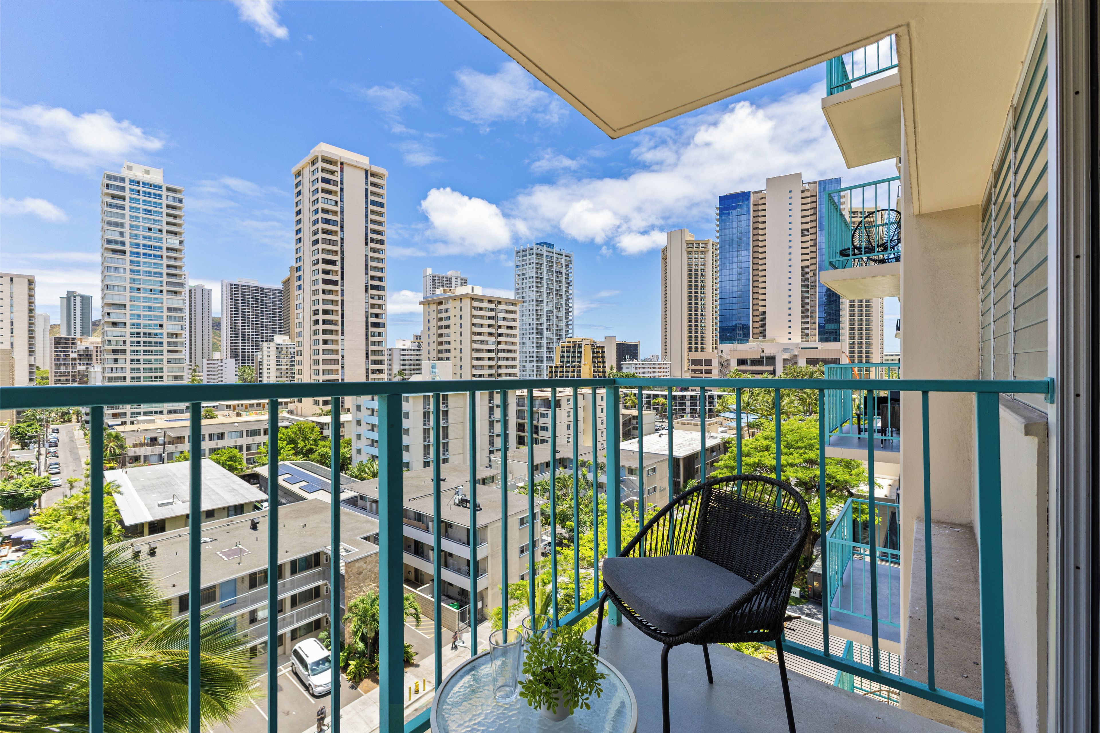 A balcony with a view of a cityscape, a chair, and a potted plant.
