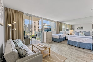 A modern hotel room with a balcony, a sofa, a bed, and a television. - Newly renovated Waikiki Studios (Honolulu)