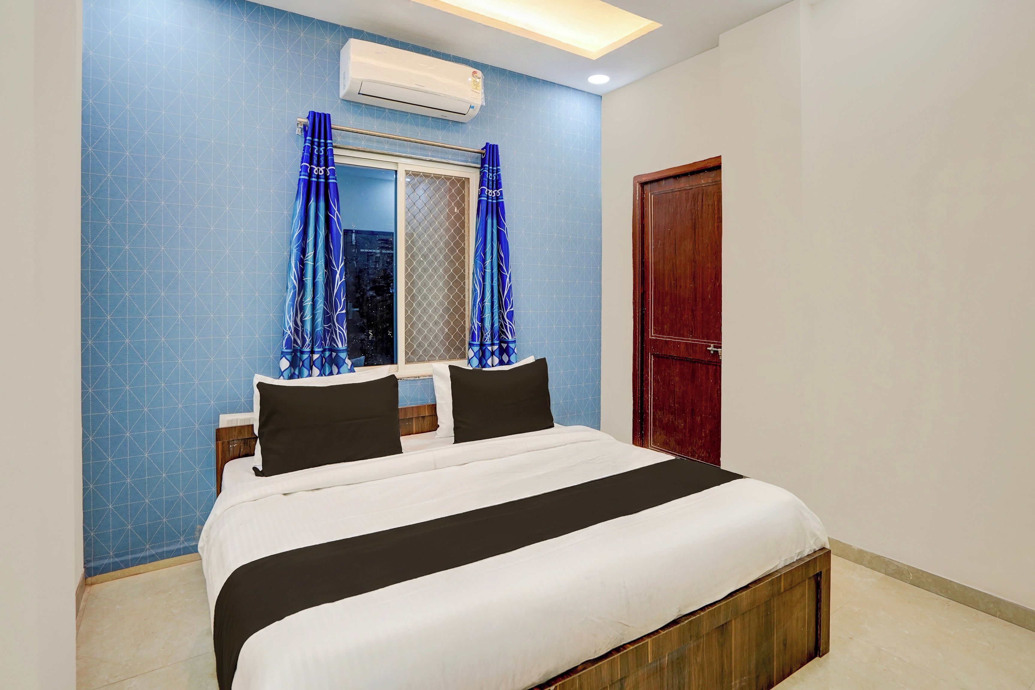 A bedroom with a bed, a window with curtains, an air conditioning unit, and a wooden door.