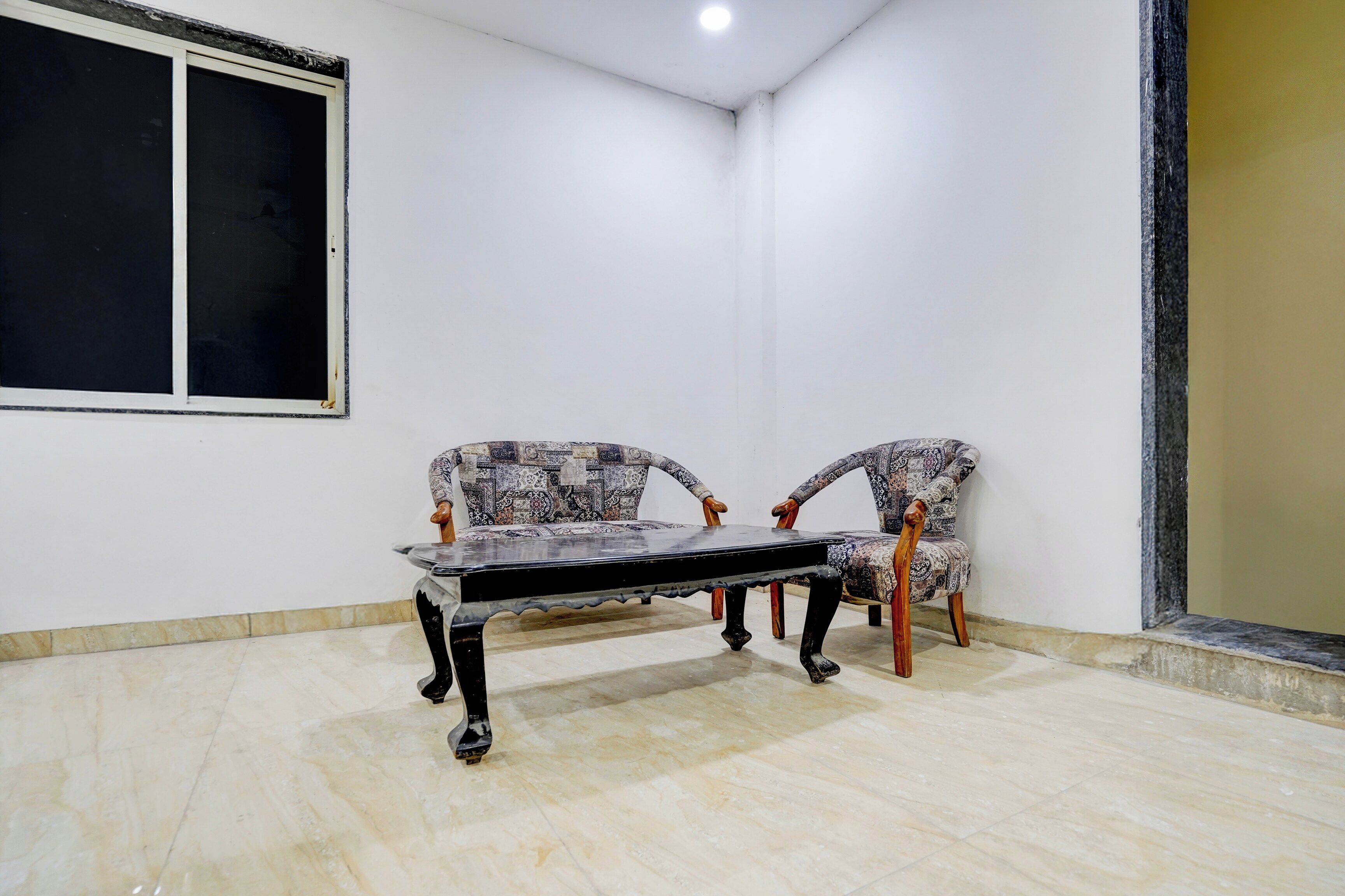 Una habitación con un ventanal grande, dos sillones estampados y una mesa.