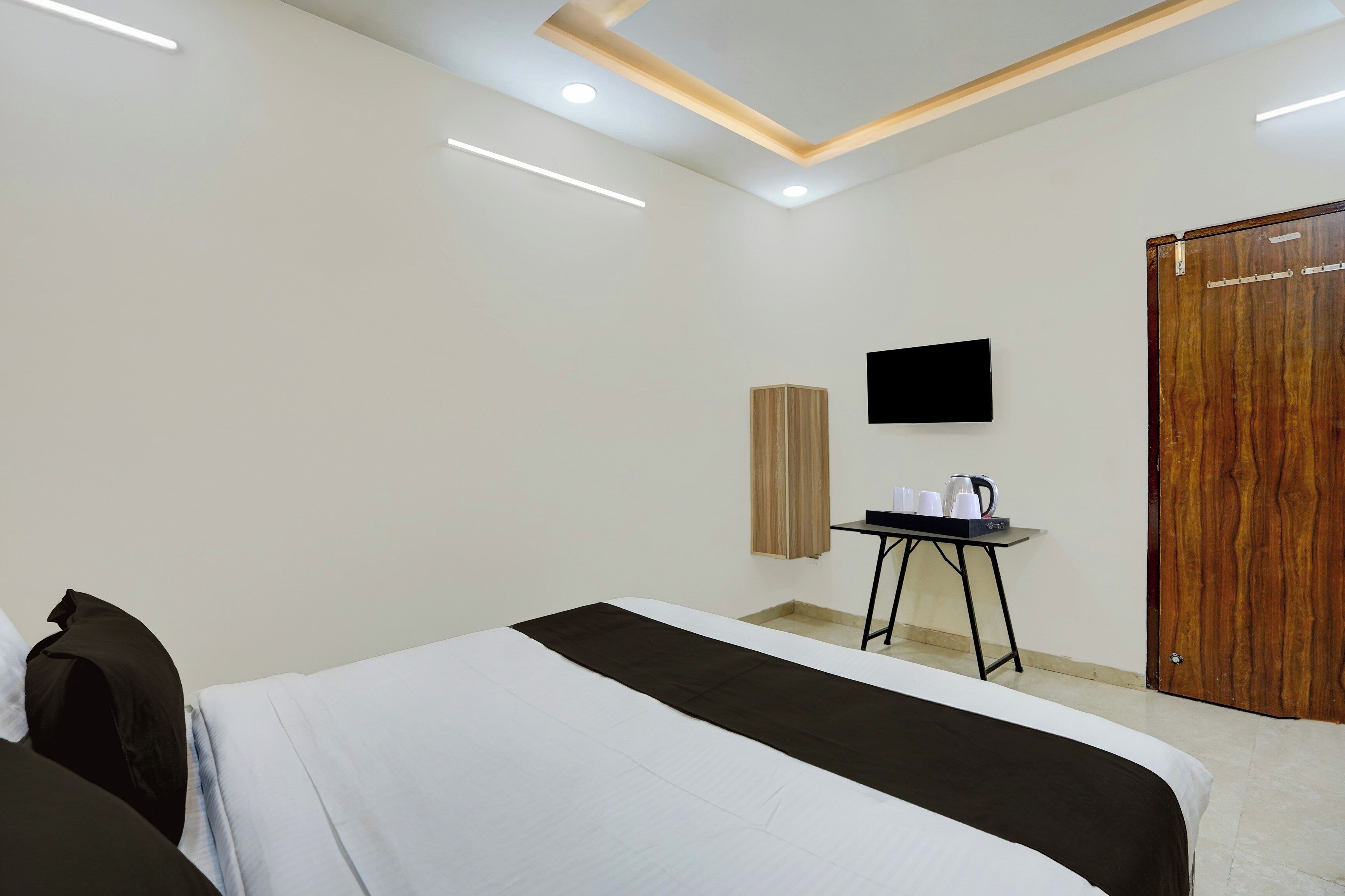 Habitación de hotel con cama, una mesita con hervidor, televisión y puerta de madera.