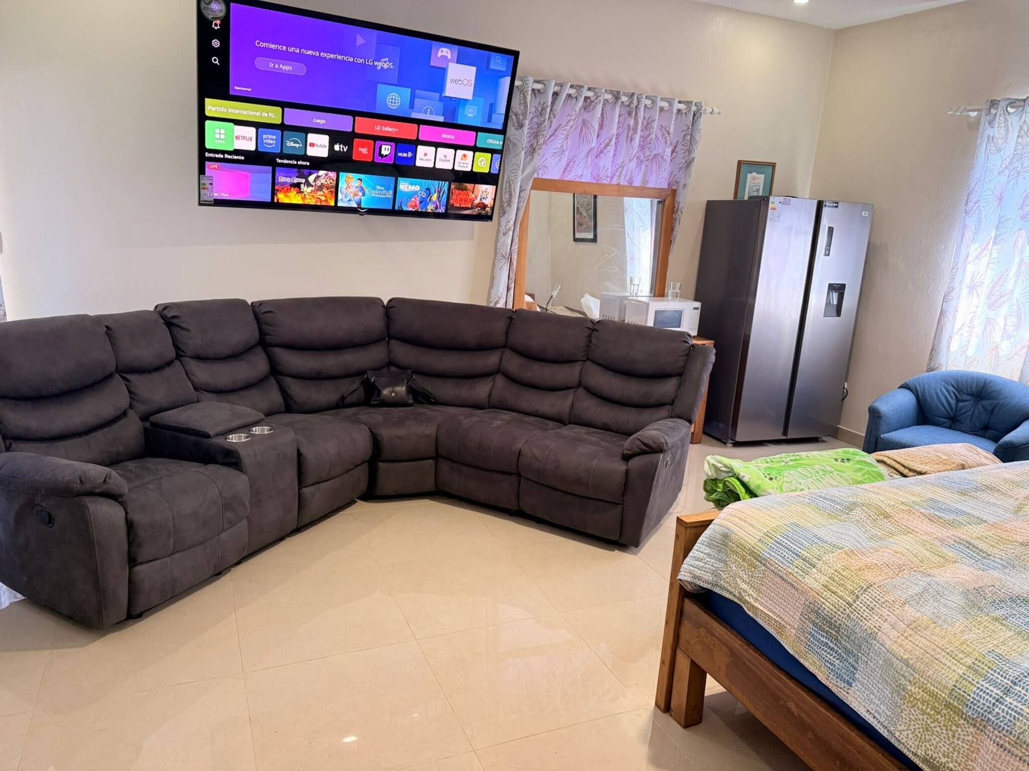 Ein modernes Wohnzimmer mit einem Ecksofa, einem Flachbildfernseher, einem Bett und einem Kühlschrank.