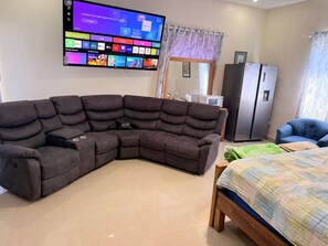 Ein modernes Wohnzimmer mit einem Ecksofa, einem Flachbildfernseher, einem Bett und einem Kühlschrank.