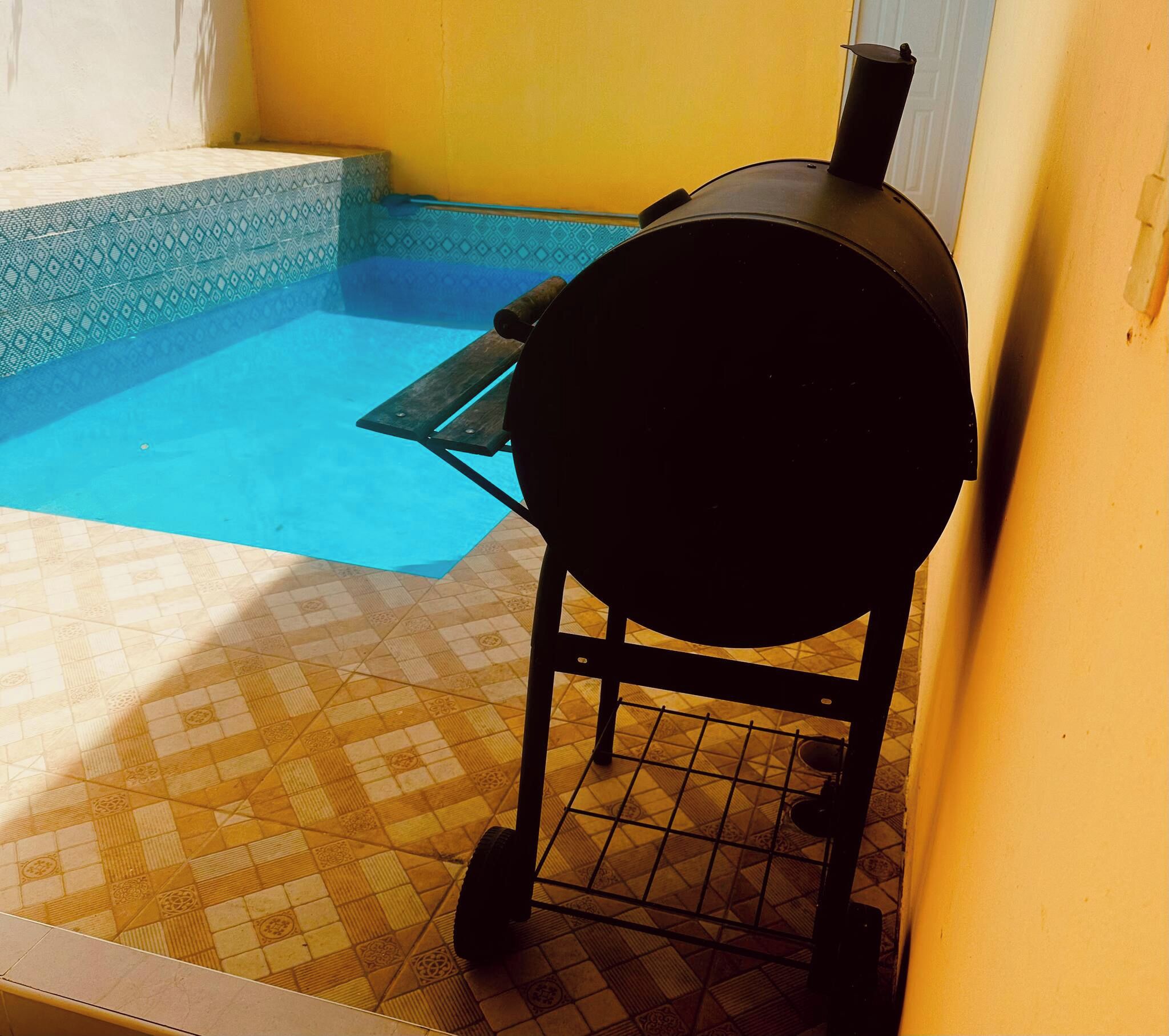 Ein Grill in der Nähe eines Schwimmbeckens mit Fliesenboden.