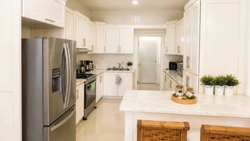 A modern kitchen with white cabinetry, stainless steel appliances, and a central island with bar stools.