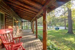 Una baita di legno con un portico, una sedia rossa e vista sulla foresta circostante.