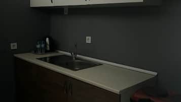 A kitchen with a white countertop, a sink, wooden cabinets, and a small refrigerator.