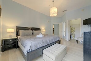 A bedroom with a bed, bedside tables, a bench, a TV, and a door leading to another room. - Huge 4th Floor Resort Condo w/Bunk Rm near Disney (Kissimmee)