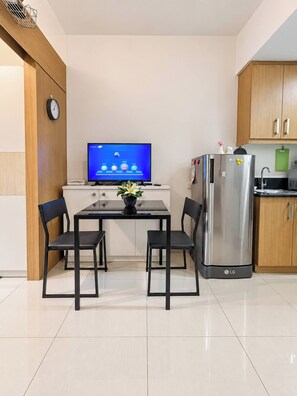 A modern kitchen with a dining table, chairs, a refrigerator, a television, and wooden cabinets. - Charming 2BR Apartment with Pool View in Vibrant Pasay City (Pasay City)