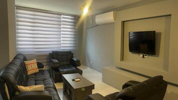 Ein modernes Wohnzimmer mit einer Sofagarnitur, einem Couchtisch und einem an der Wand befestigten Flachbildfernseher.