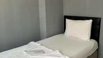 Ein Einzelbett mit weißer Matratze und Kissen, einer weißen Tagesdecke und einem Kopfteil.