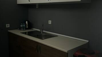 Eine Küche mit weißer Arbeitsplatte, einem Spülbecken, Holzschränken und einem kleinen Kühlschrank.