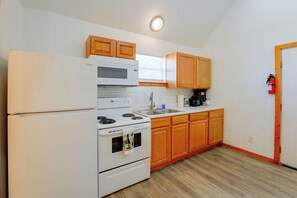 A kitchen with a refrigerator, stove, microwave, wooden cabinets, and a fire extinguisher. - Walk to Main St! Group-Friendly Stockdale Getaway (Stockdale)