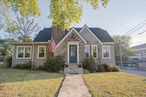 A single-story house with a stone facade, a front porch, and a flag. - Explore Scenic City | Cozy Getaway | Sleeps 8! (Chattanooga)