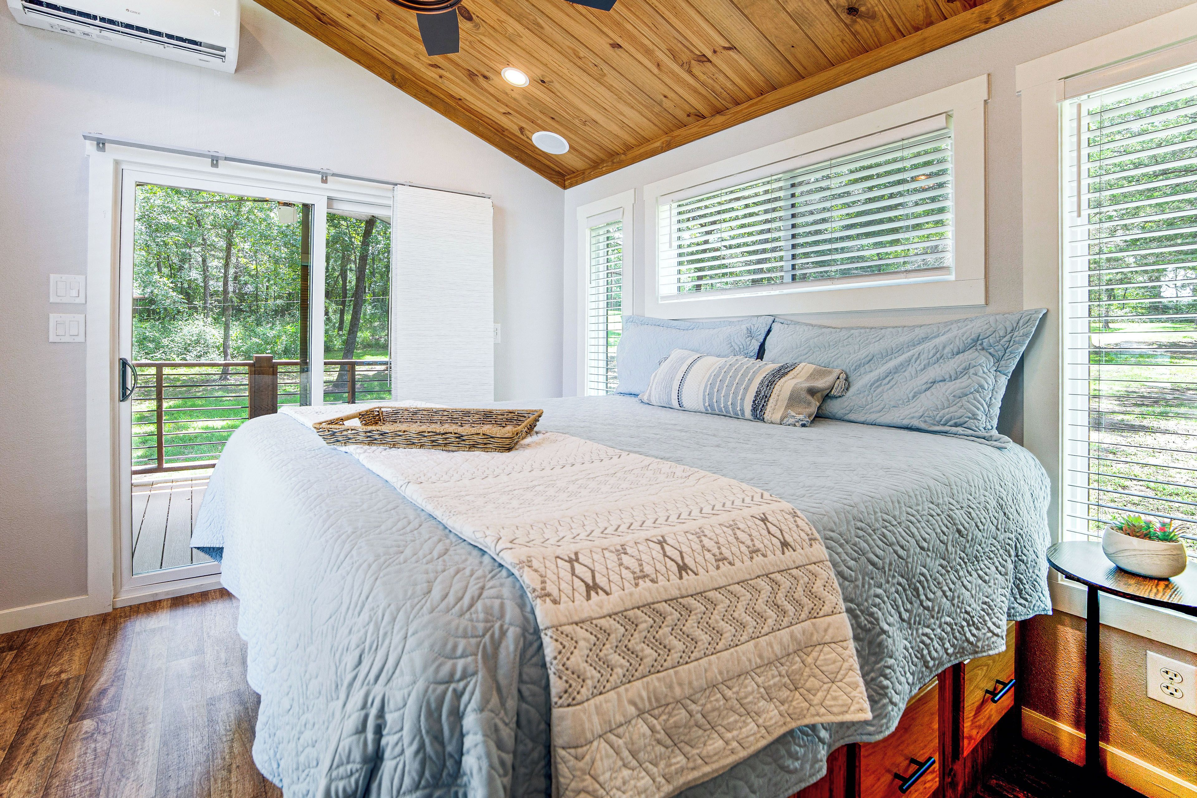 A bedroom with a large bed, a wooden ceiling, and a view of greenery outside.