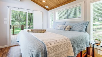 A bedroom with a large bed, a wooden ceiling, and a view of greenery outside.