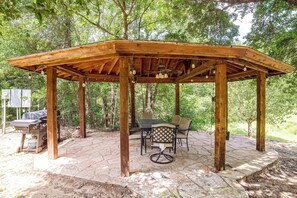 A wooden gazebo with a table and chairs, surrounded by a stone patio. - Lakefront Hot Tub/Swim Spa, Peaceful Paradise Cove (Streetman)