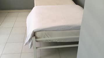 A single bed with a white mattress and pillow in a room with grey walls and tiled flooring.