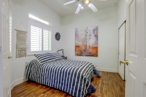 Ein Schlafzimmer mit einem Bett, einem Fenster mit Jalousien, einem Deckenventilator, einem Wandbild und einer Tür mit Schlüsselloch.