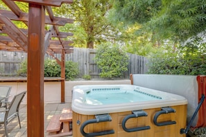 Uma banheira de hidromassagem com estrutura de madeira e tampa branca, cercada por uma pérgola de madeira e um cercado de madeira.