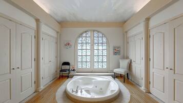 A spacious bathroom with a freestanding bathtub, a large arched window, and a white tiled floor.