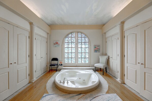 A spacious bathroom with a freestanding bathtub, a large arched window, and a white tiled floor.