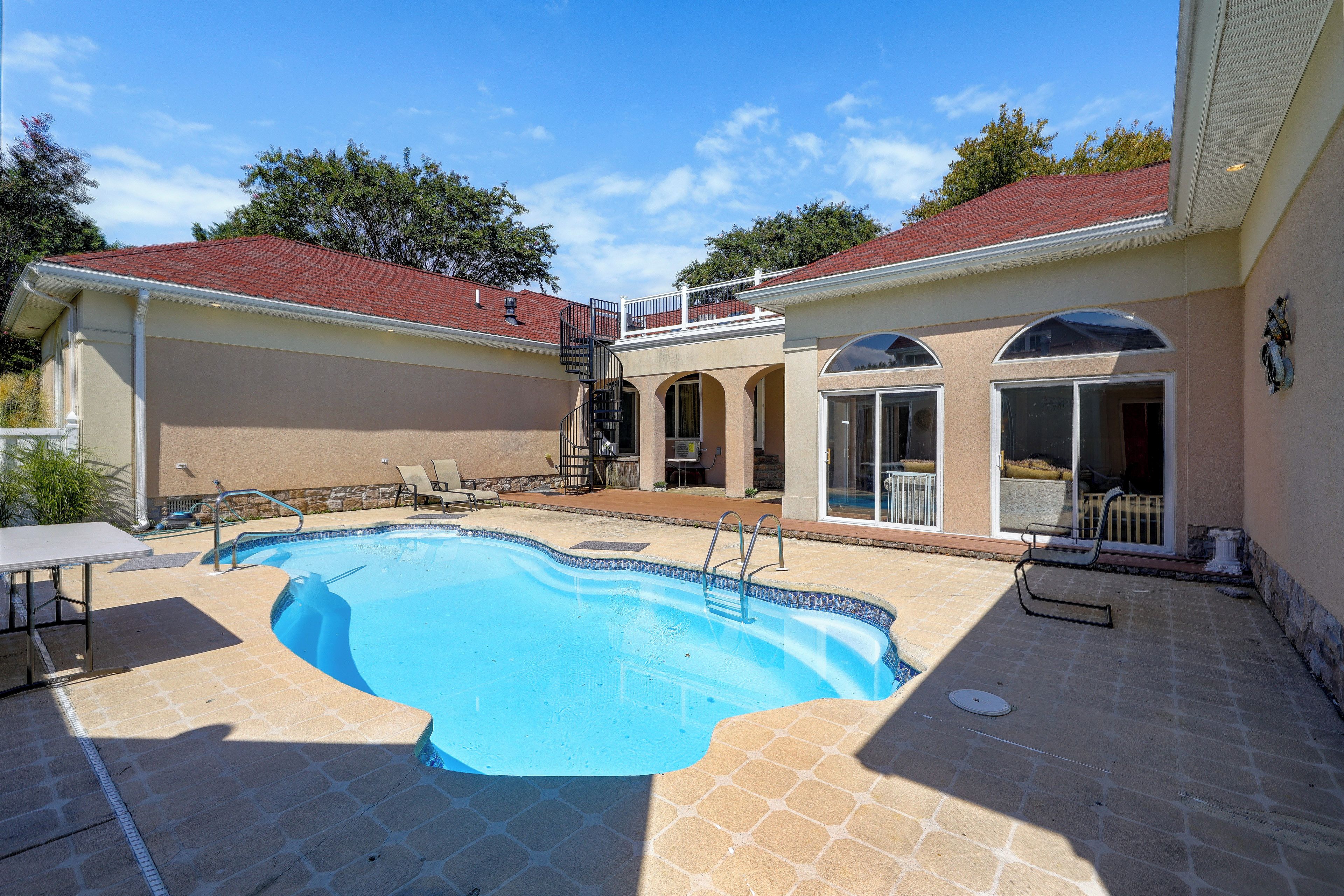 A backyard with a swimming pool, a covered patio area, and a separate building with a red roof.