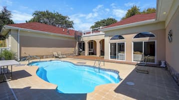 A backyard with a swimming pool, a covered patio area, and a separate building with a red roof.