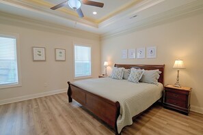 Ein Schlafzimmer mit einem hölzernen Bett, zwei Nachttischen mit Lampen, einem Deckenventilator und gerahmten Pflanzenbildern an der Wand.