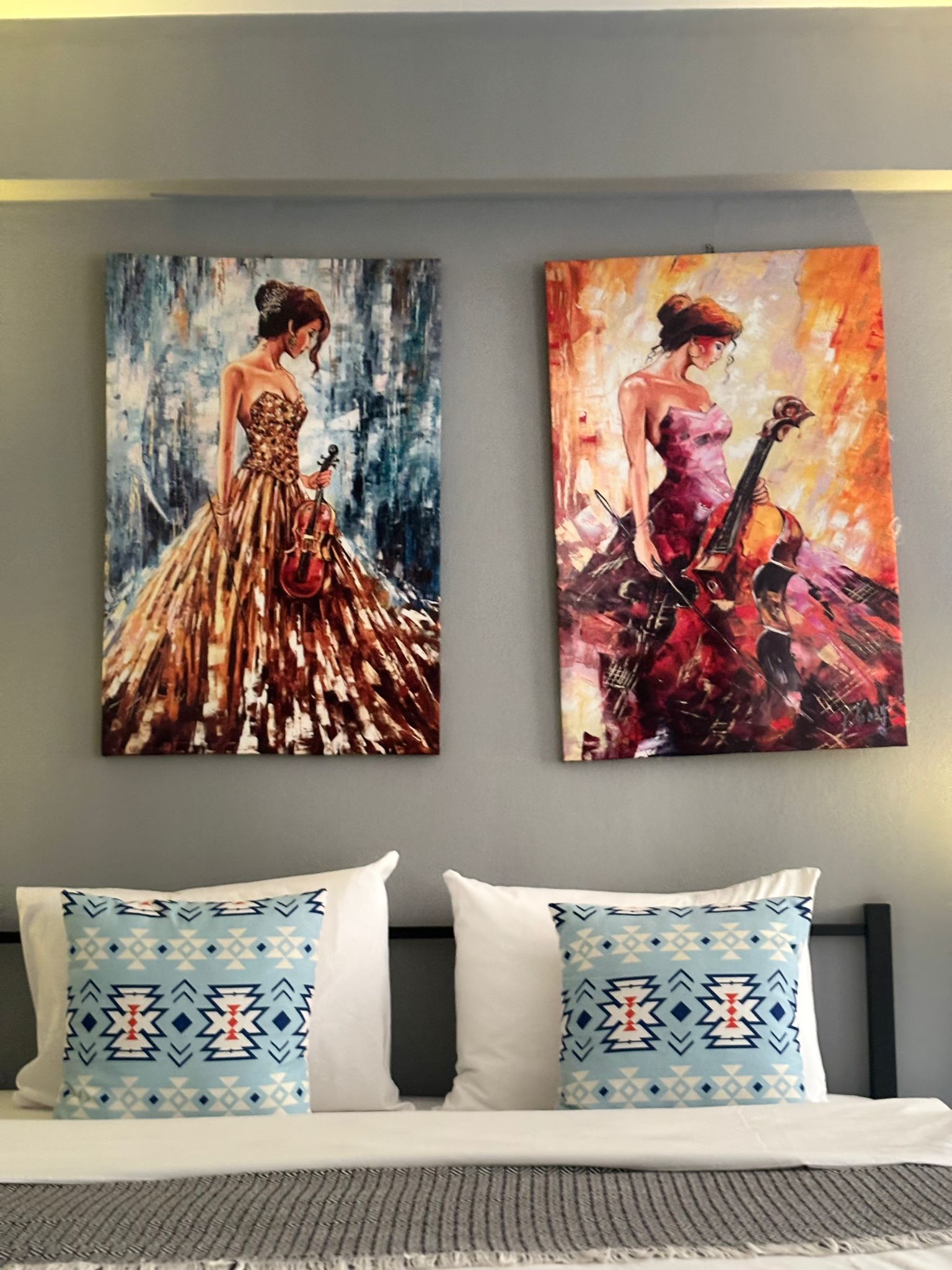 Deux tableaux accrochés au mur au-dessus d’un lit, avec des coussins à motifs.