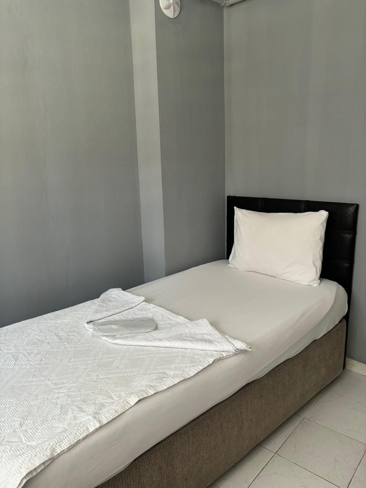 A single bed with a white mattress and pillow, a white throw blanket, and a headboard.