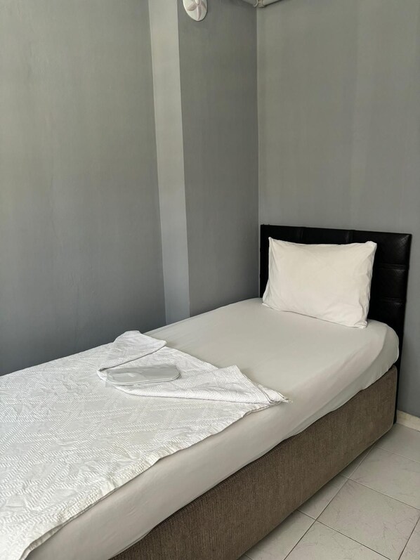 Una cama individual con colchón y almohada blancos, y una manta suave blanca, además de un cabecero.
