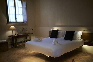 Habitación de hotel con una cama grande, un escritorio con lámpara, una silla y una ventana con cortinas.
