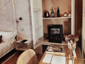 A hotel room with a bed, a bedside table with a phone, a small table with a vase of flowers, a shelf with bottles, and a refrigerator. - Badia Giulia - Adults Only (Camaiore)